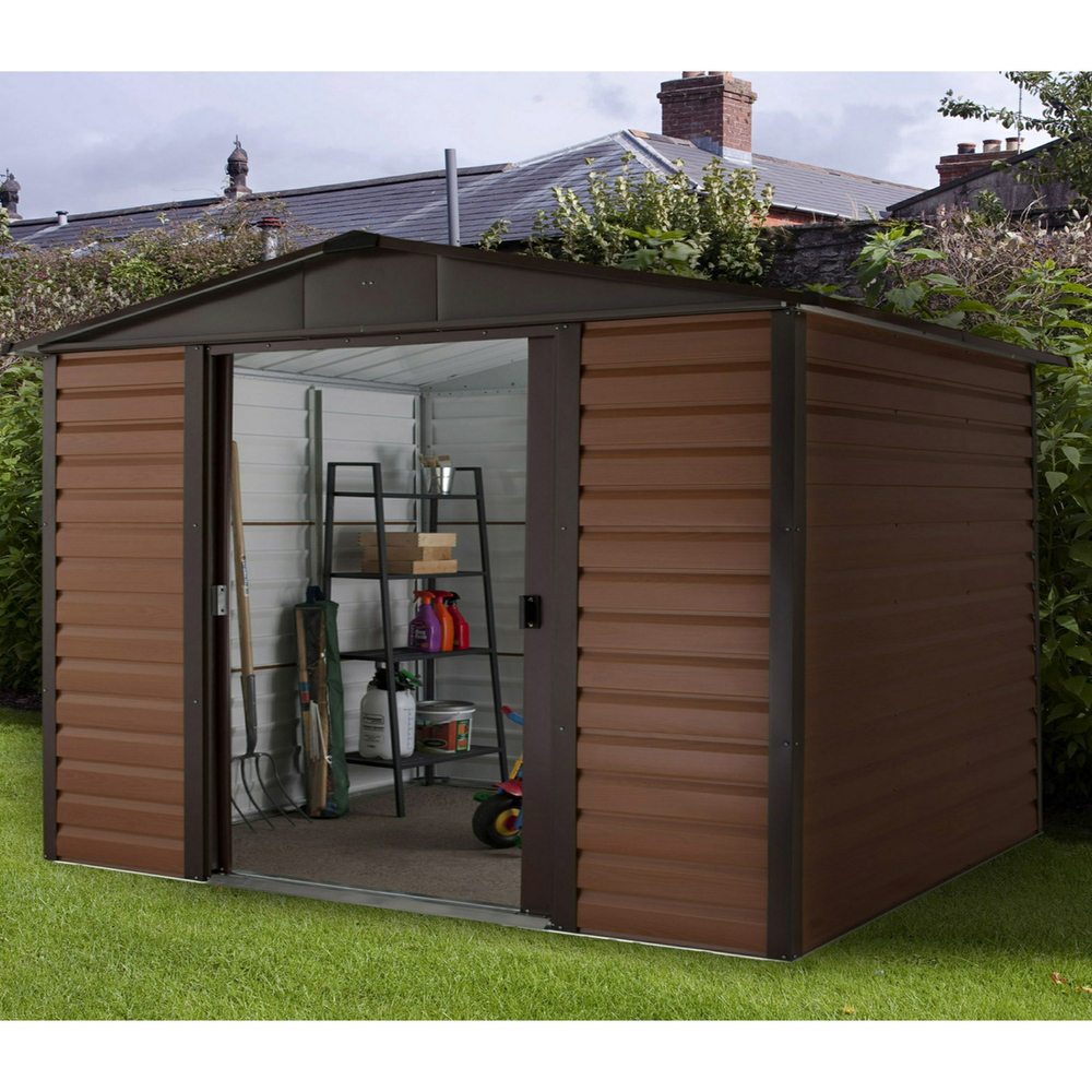 Brown metal shed with woodgrain finish, featuring a sloped roof, double doors, and a floor support frame, set in a garden with tools and shelving visible inside.