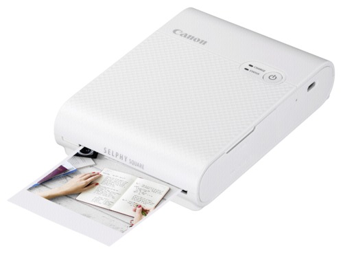 Canon SELPHY SQUARE QX10 portable wireless photo printer in white, featuring a textured surface and a print emerging from the front, showcasing vibrant color output.