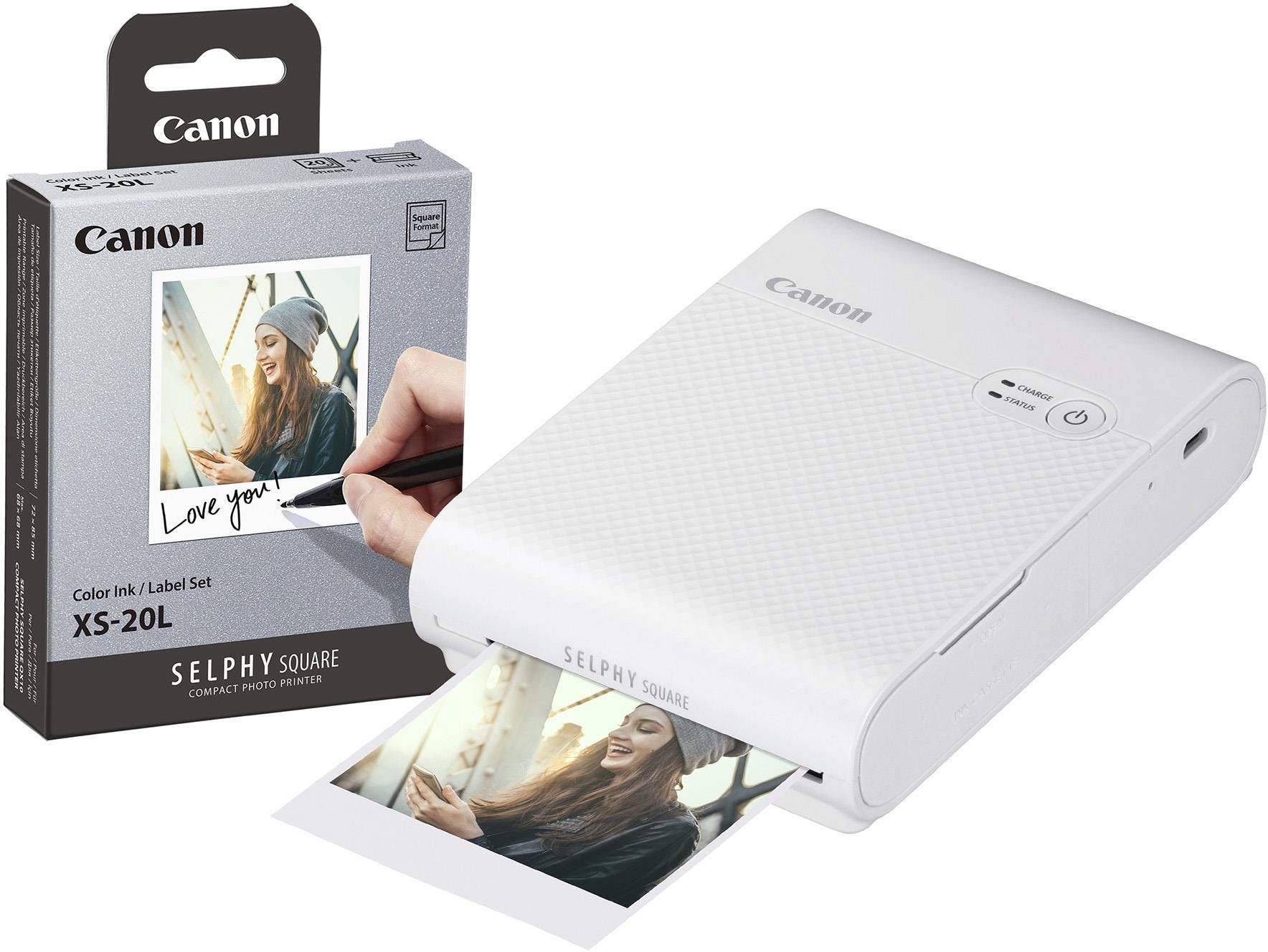 Compact white Canon Selphy Square QX10 wireless photo printer with a textured surface, featuring a printout of a smiling woman and a box of color ink and labels.