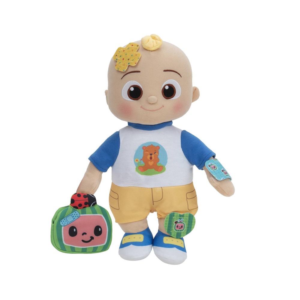 Boo Boo JJ Interactive Doll features a soft, plush body, wearing a blue shirt with a cartoon character, yellow pants, and carrying a green bag with a smiling face.