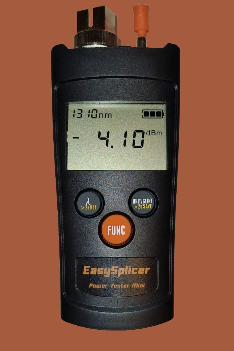 Black handheld device with a digital display showing 1310nm and -4.10dBm, featuring orange buttons labeled "FUNC" and "UNIT/LIMIT," and a fiber optic connector on top.
