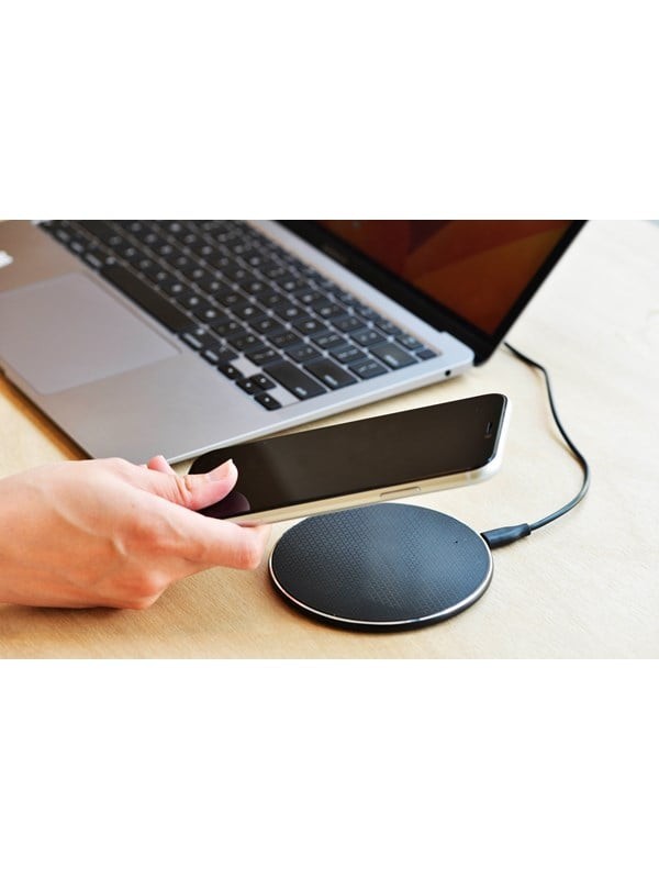 Black Energizer 15W QI wireless charging pad with a textured surface, featuring a sleek design and a silver edge, placed beside a laptop and a hand holding a smartphone.