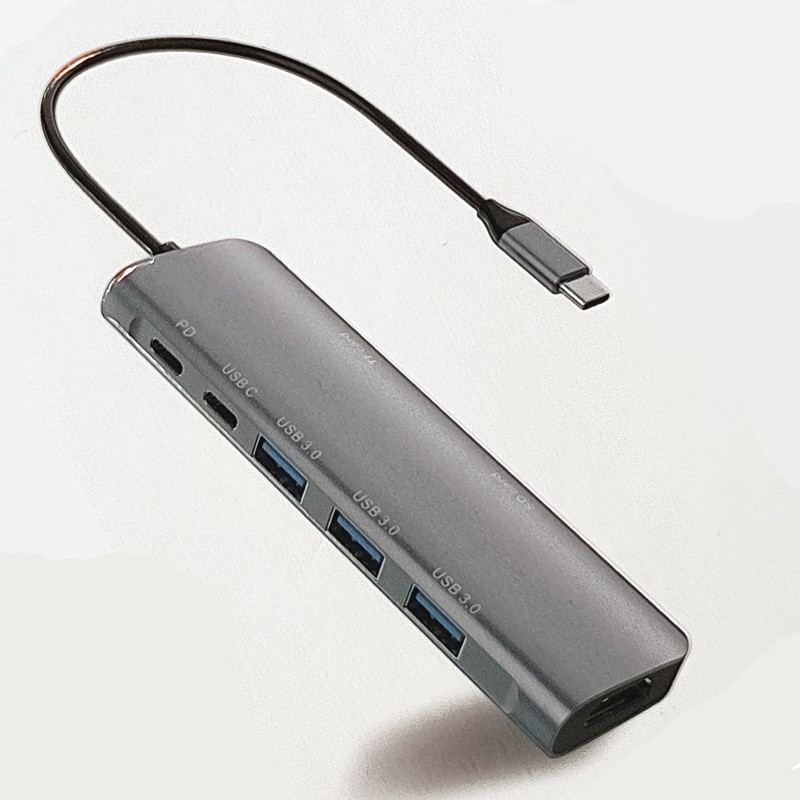 Silver aluminum USB-C hub featuring HDMI, two USB-A ports, two USB-C PD & data ports, and two SD card slots, with a short USB-C cable attached.