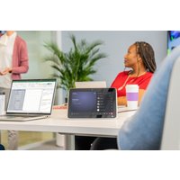 HP Poly TC10 black glass mount with touchscreen, showing interface, on a conference table with laptops and people nearby.