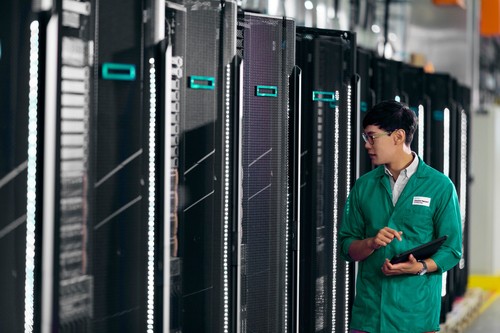 A technician in a green jacket inspects black server racks with teal accents, featuring LED lights and a sleek design in a modern data center.