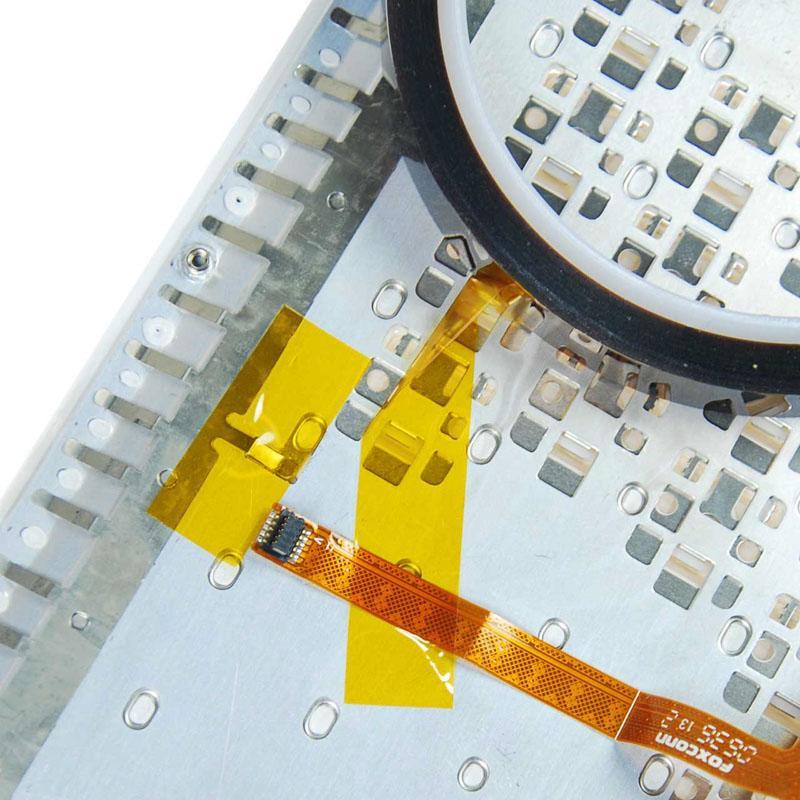 Yellow polyimide tape is applied to a metallic surface, with a flexible orange ribbon cable and a circular black component visible in the background, showcasing its heat-resistant properties.