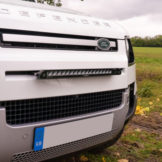 Lazer Lamps Grille Integration Kit featuring a sleek black Linear 18 lamp mounted on a white Land Rover Defender's grille, set against a natural outdoor backdrop.