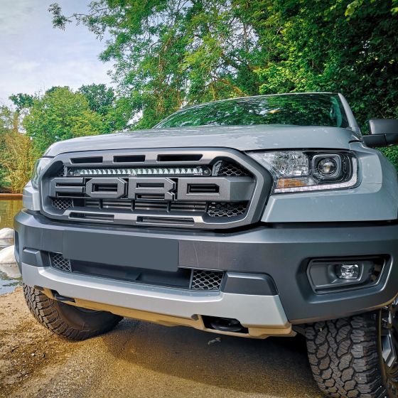 Lazer Lamps Grille Integration Kit featuring a sleek black Linear 24 Elite Lamp mounted on a silver Ford truck's grille, set against a lush green background.