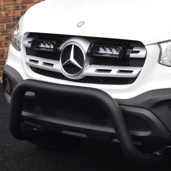 Lazer Lamps Grille Integration Kit featuring two black Triple-R 750 lamps mounted on a silver grille of a white vehicle, complemented by a black bull bar.