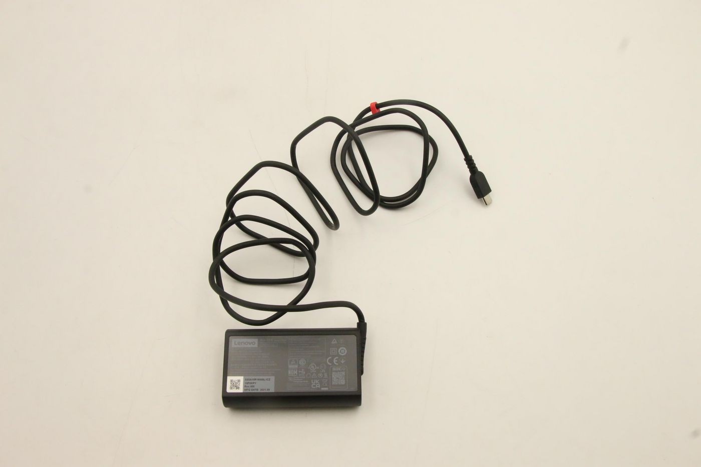 Black Lenovo 65W USB-C power adapter with a textured surface, featuring a coiled black cable and a red connector tip.