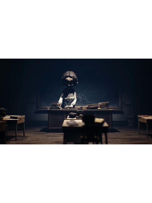 A dark classroom scene from "Little Nightmares II," featuring a large, ominous figure at a desk, surrounded by empty student desks, creating a tense atmosphere.