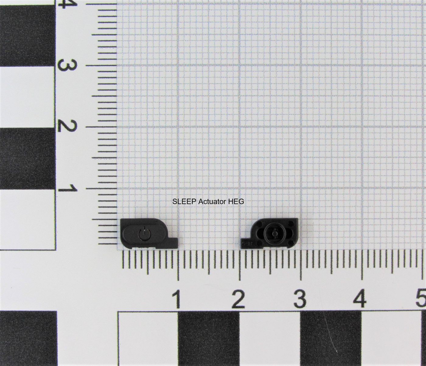 Black Nintendo C/SLEEP(K1) HEG actuator, featuring a compact design with a circular button and a small lens, placed on a grid background for scale.