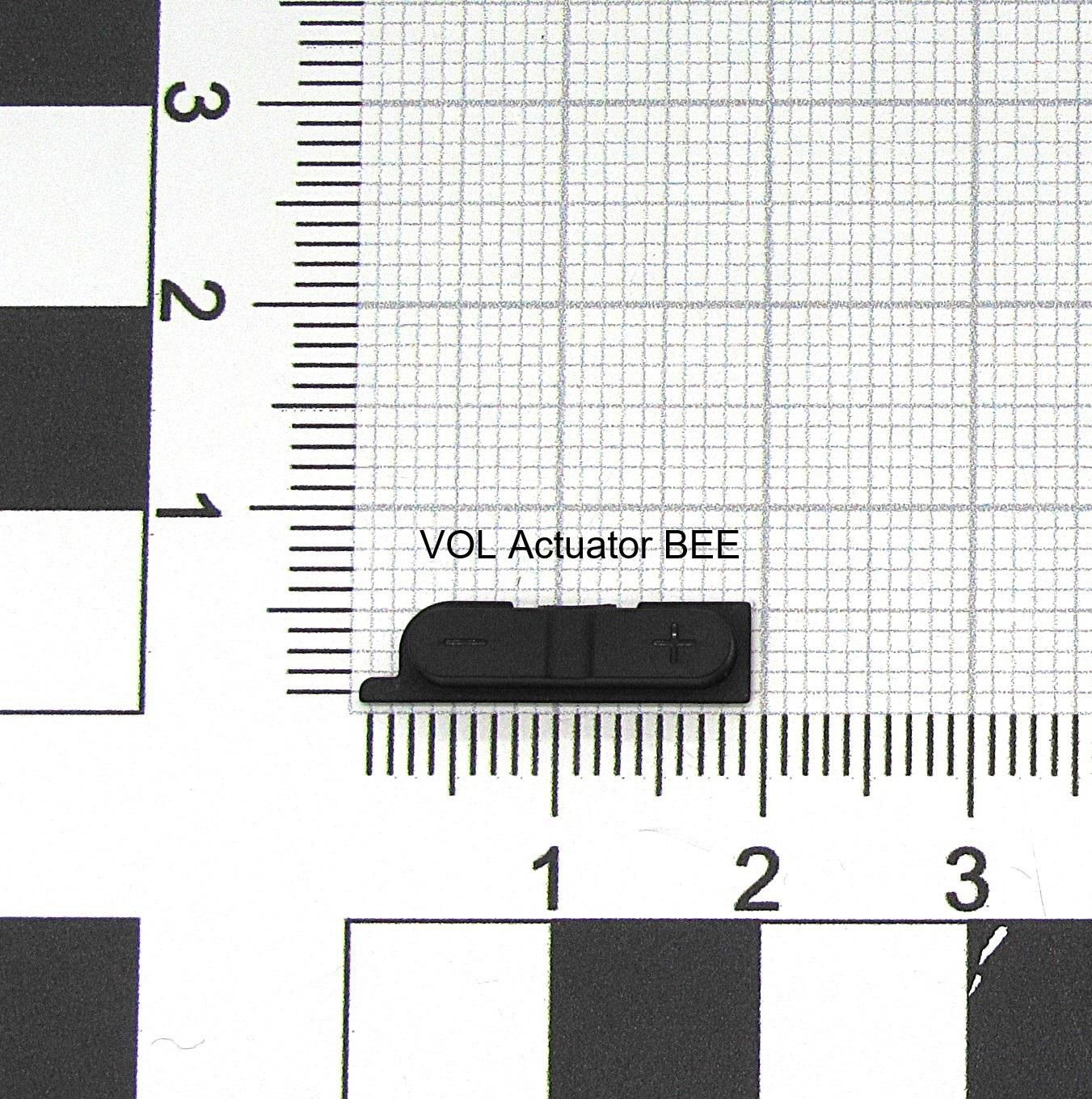 Black plastic VOL actuator with a small rectangular shape, featuring a "+" symbol, placed on a grid background with measurement markings.