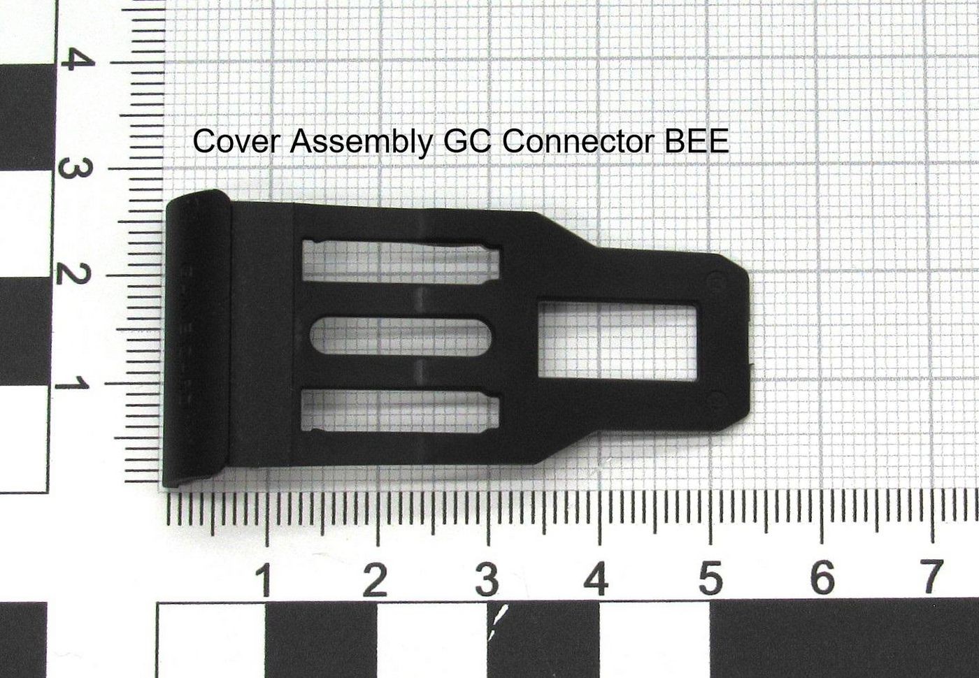 Black plastic cover assembly connector with three vertical slots and a flat top, measuring approximately 5 cm in length, set against a grid background for scale.