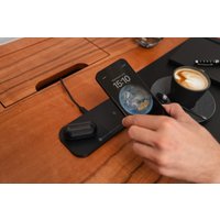 Black dual wireless charging pad with two devices charging, sleek design, wooden desk background.