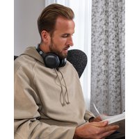 Black over-ear Bluetooth headphones with cushioned ear cups and adjustable headband worn by a person in a beige hoodie.