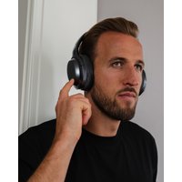Black over-ear Bluetooth headphones with cushioned ear cups and sleek design worn by a person touching the right ear cup.