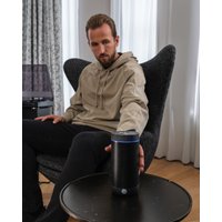 Black cylindrical Bluetooth speaker with blue LED ring on top, placed on a round black table.