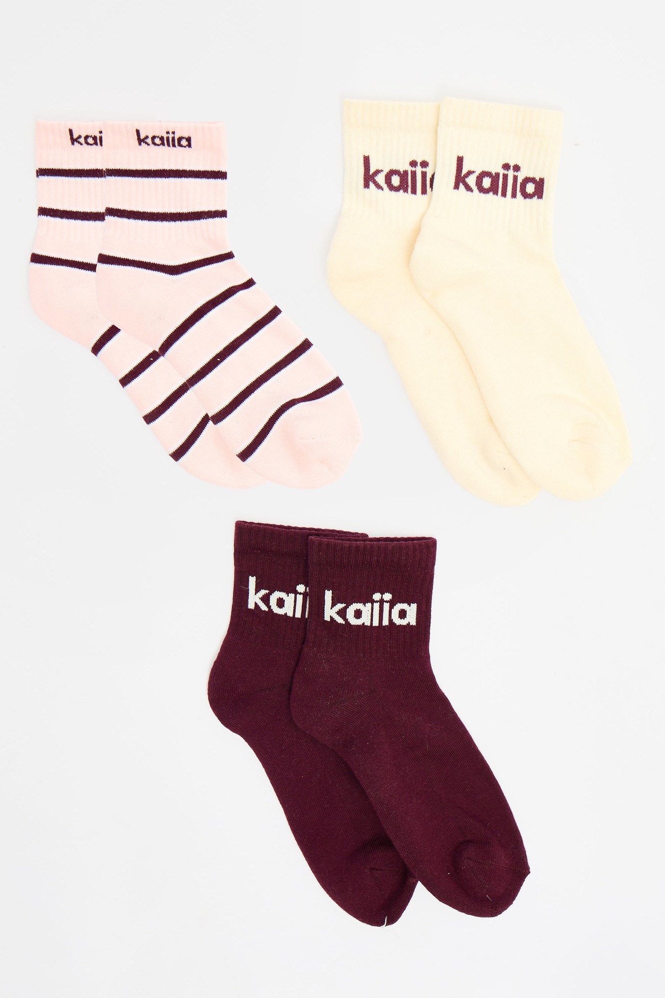 Three pairs of Kaiia socks in pink with burgundy stripes, cream, and burgundy, featuring the brand name "kaiia" in contrasting text on each pair.