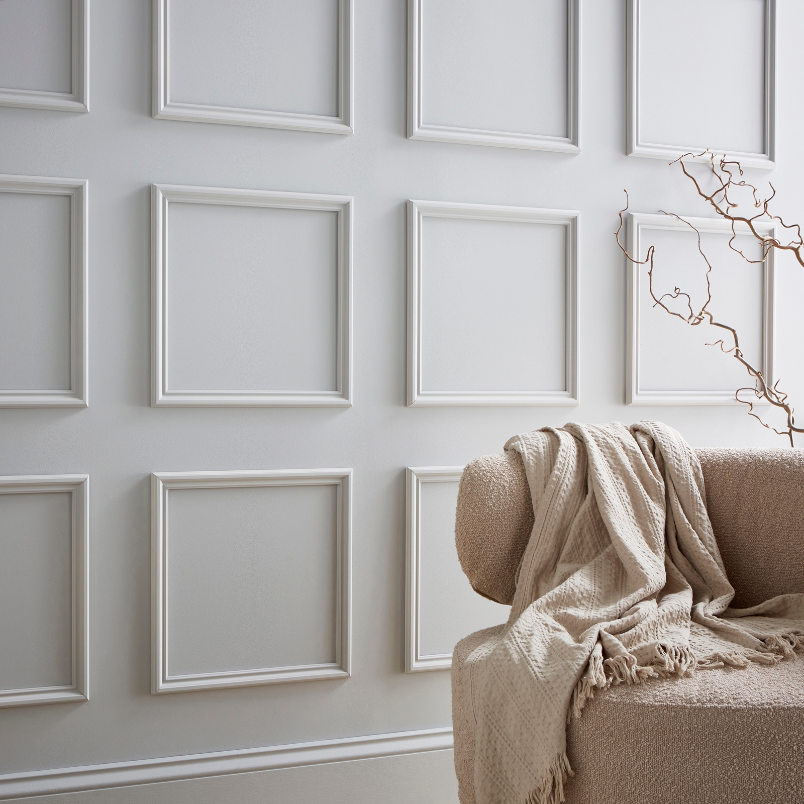 White wall panel kit featuring a mix of rectangular frames, designed for easy installation, complemented by a textured beige sofa and a soft throw blanket.