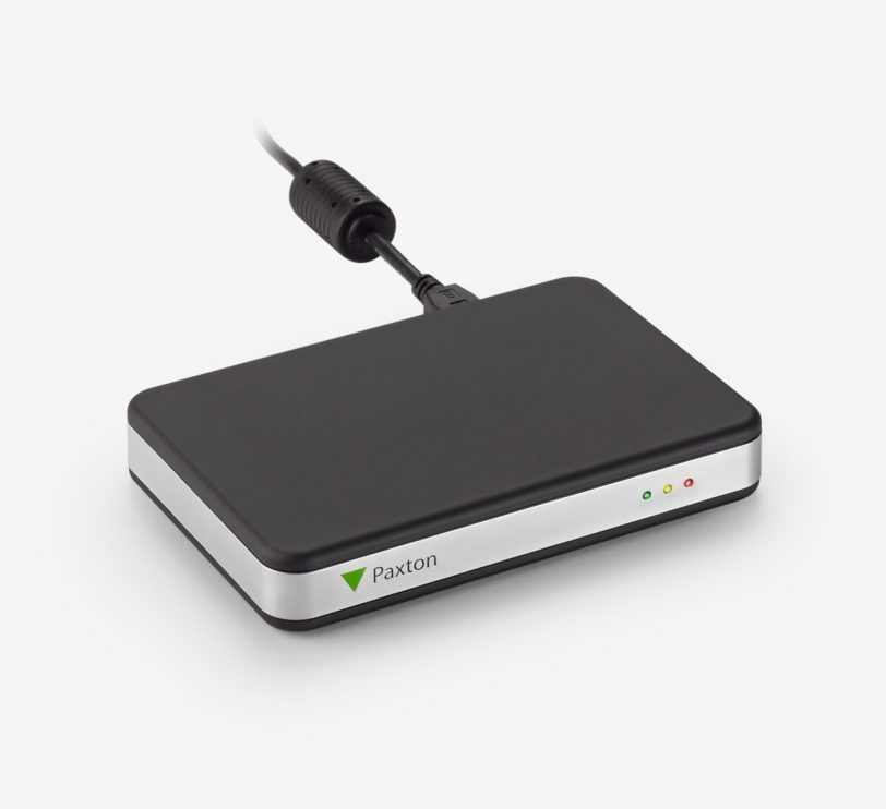 Black rectangular desktop reader with a silver edge, featuring a USB connection and two indicator lights (red and green) on the front, branded with the Paxton logo.