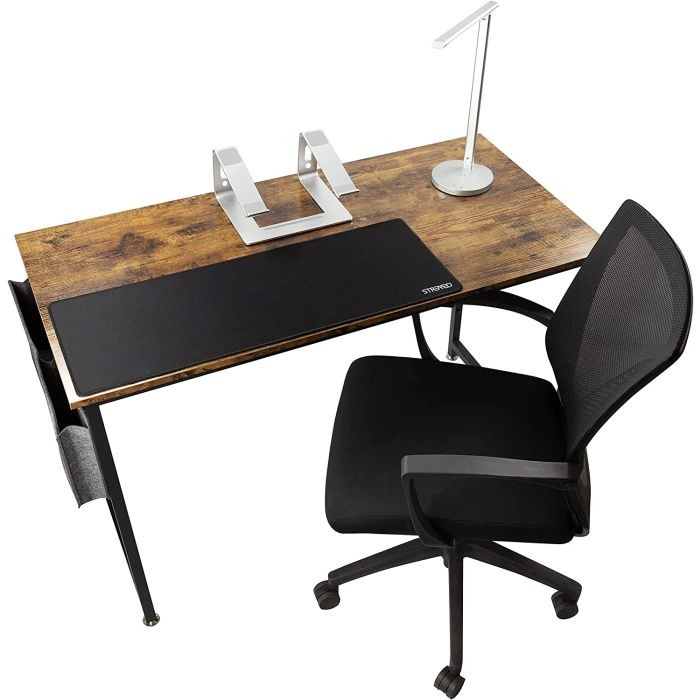 Wooden desk with a dark surface, a sleek silver lamp, a black desk mat, and a black ergonomic chair with mesh back, all arranged for a productive work-from-home setup.