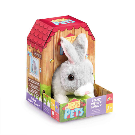 Grey and white plush bunny toy with large ears, sitting in a colorful cardboard box featuring a red roof and playful graphics, designed for children aged 3 and up.