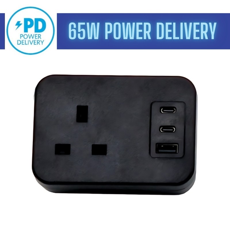Black desktop power adapter featuring one power socket, dual USB-C ports, and a USB-A port, labeled with "65W Power Delivery" in blue.