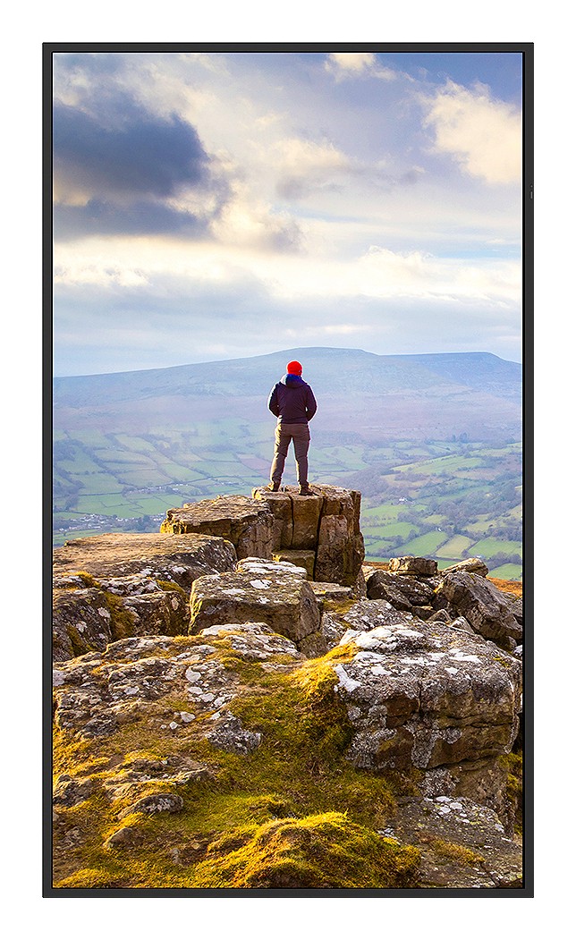 Sharp PN-E439 digital signage flat panel features a sleek black frame, 43-inch LCD display, and a vibrant image showcasing a person standing on a rocky outcrop against a scenic landscape.