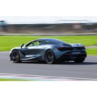 Gray McLaren 720S supercar speeding on a racetrack, showcasing sleek aerodynamic design and distinctive rear spoiler.