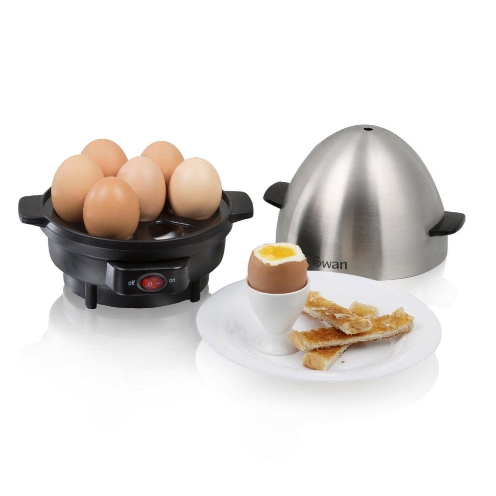 Swan egg cooker in black with a stainless steel dome, holding six brown eggs, accompanied by a soft-boiled egg in a white cup and toast strips on a plate.
