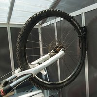 Black Palram Canopia vertical bicycle hanger holding a bike by its front wheel in a metal-framed space.