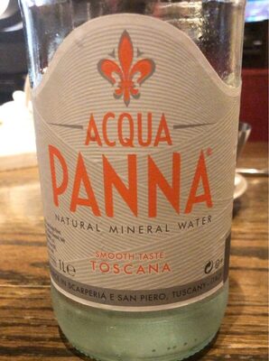 Clear glass bottle of Acqua Panna still mineral water, featuring a prominent red logo and a decorative orange fleur-de-lis, labeled "Natural Mineral Water" and "Smooth Taste Toscana."