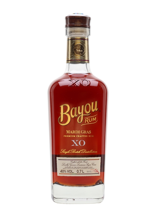 Clear glass bottle of Bayou XO Mardi Gras Rum, featuring a deep amber liquid, gold lettering, and a cork stopper, with a label detailing its premium crafted quality.