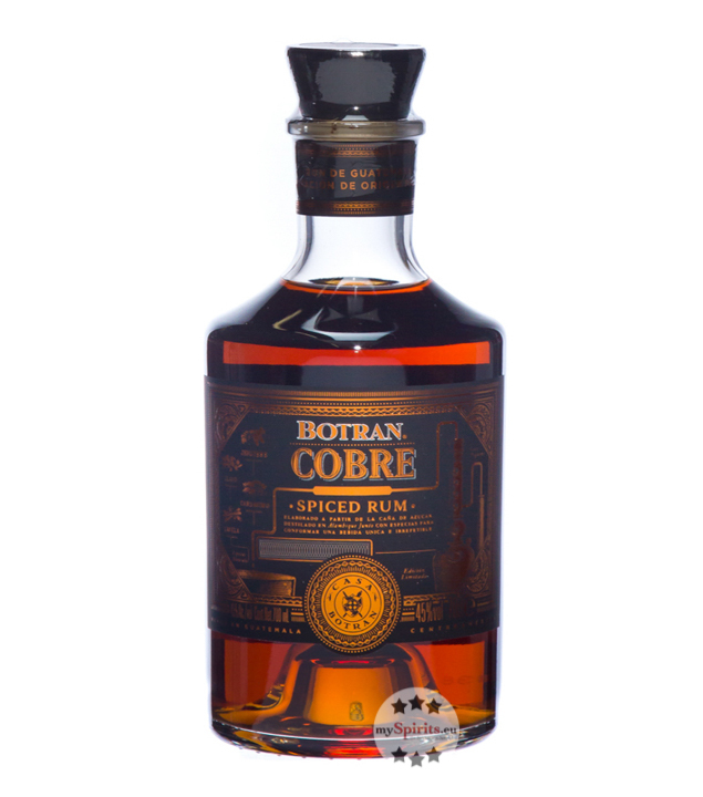Botran Cobre Spiced Rum bottle features a dark amber liquid, a round glass shape, a black cork stopper, and gold and blue labeling with intricate designs.