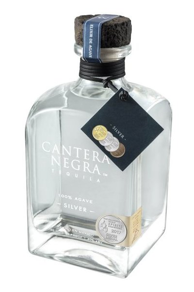 Clear glass bottle of Cantera Negra Silver Tequila, 75 cl, featuring a cork stopper, a blue ribbon, and a black tag with silver and gold medals, labeled "100% Agave Silver."