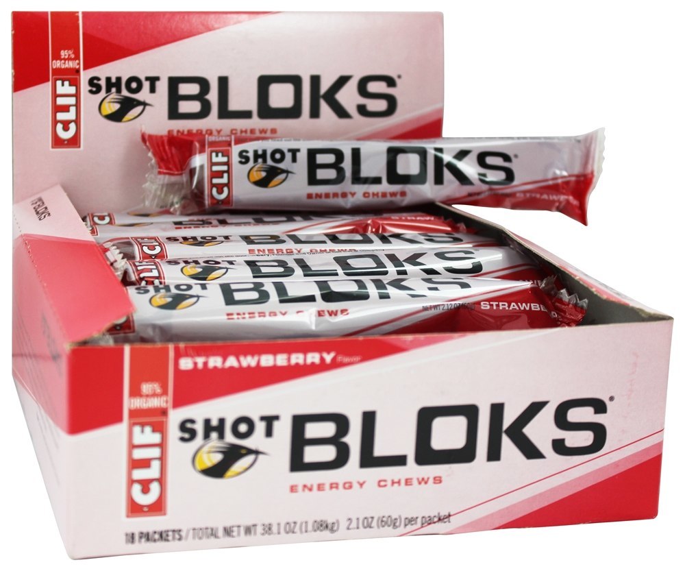 Red and white box of CLIF Shot Bloks energy chews, featuring a strawberry flavor, with individual packets visible inside, emphasizing the brand logo and organic label.