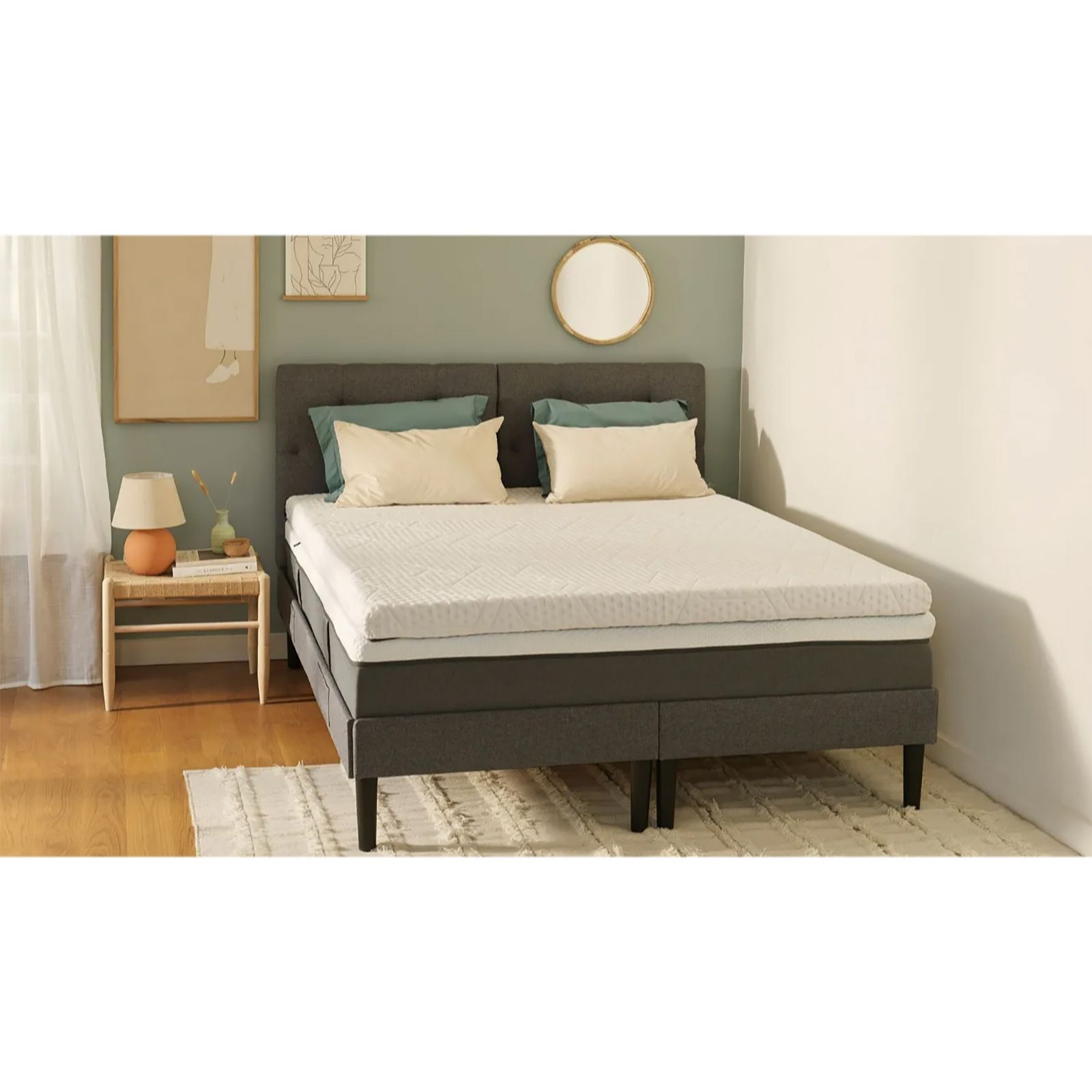 The Emma Original Pro Topper features a white quilted surface, soft foam material, and is placed on a stylish gray bed frame with two decorative pillows and a bedside table.