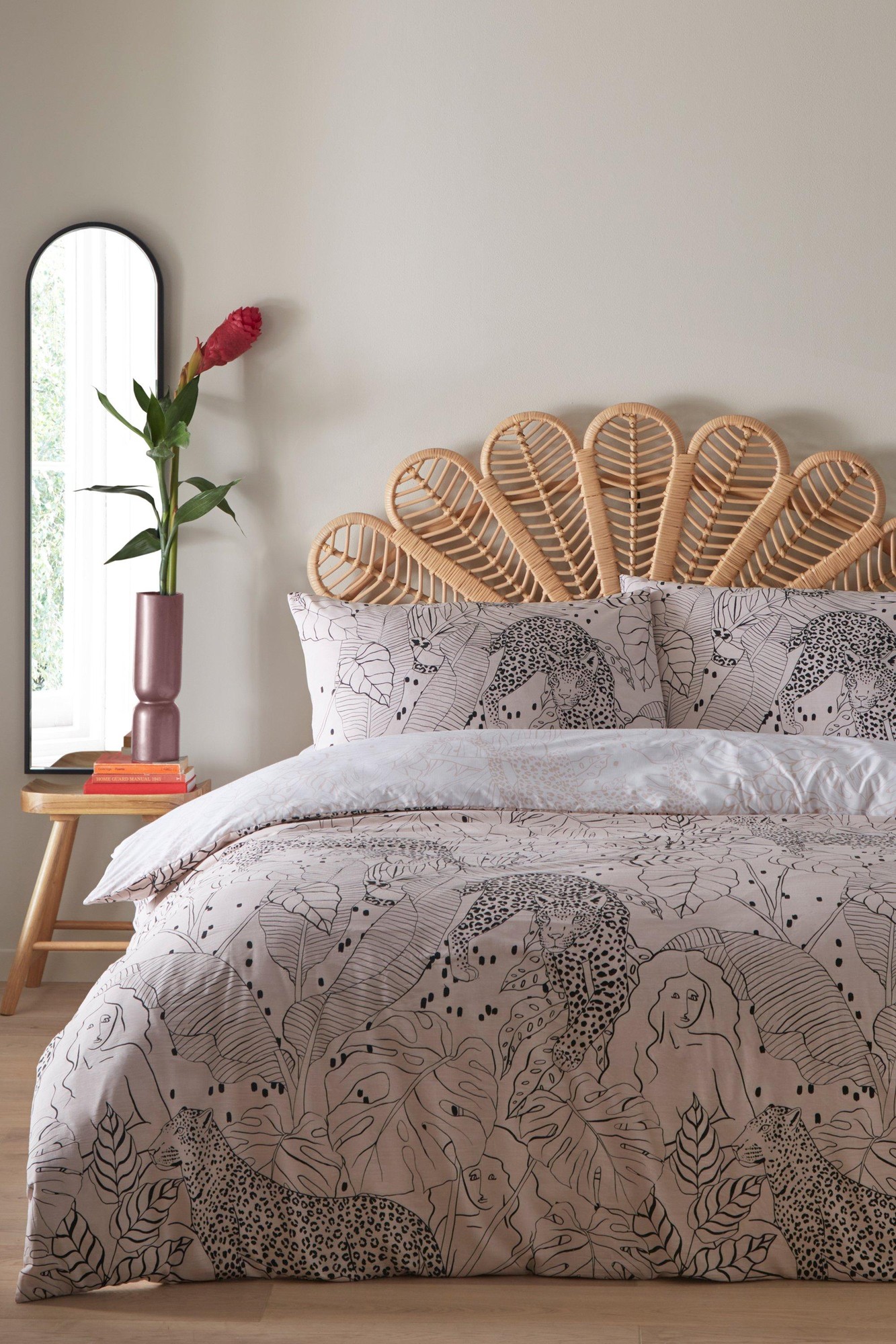 Blush cotton duvet cover set featuring tropical jungle prints with black outlines, complemented by a rattan headboard and a decorative mirror and vase in the background.