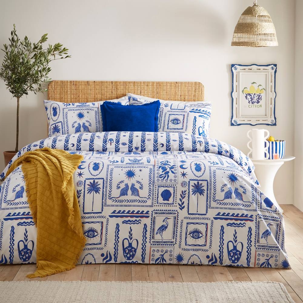 Double duvet cover set in pink and blue polycotton featuring an abstract frieze design, complemented by a textured yellow throw and decorative pillows on a woven headboard.