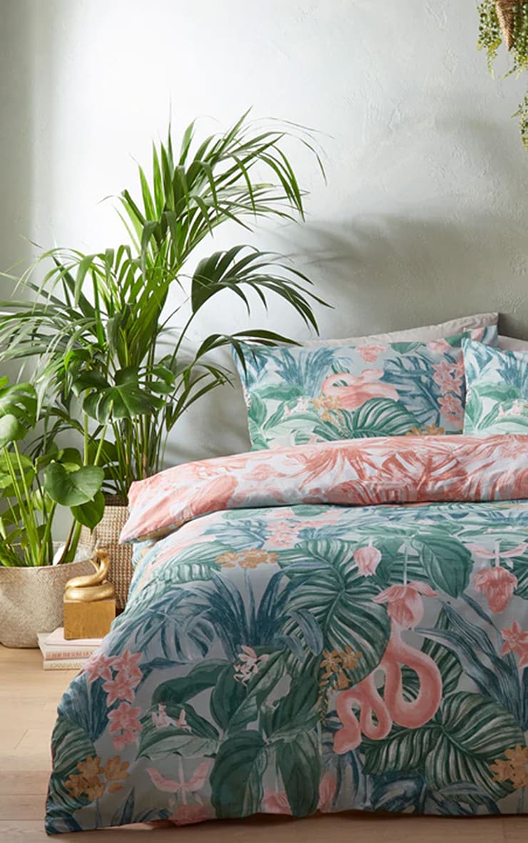 Tropical reversible duvet cover set in mint cotton featuring vibrant pink and green foliage, complemented by matching pillowcases, styled with indoor plants.