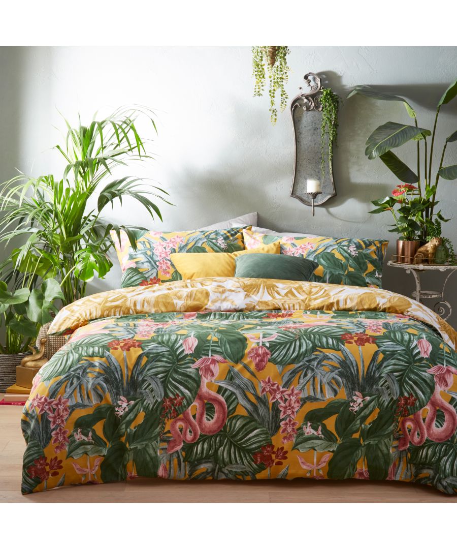 Tropical reversible duvet cover set in mustard cotton with vibrant floral and foliage patterns, complemented by coordinating pillows and lush greenery in the background.