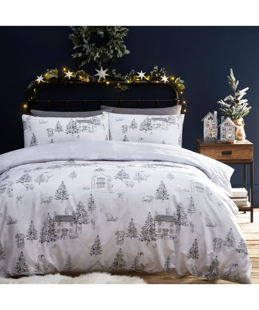 Festive reversible duvet cover set in white with a toile design featuring winter scenes, trees, and cabins, paired with matching pillowcases, suitable for a king-sized bed.