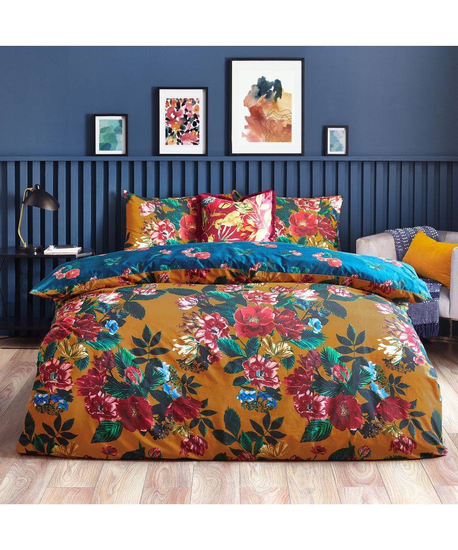 Botanical Nadya reversible duvet cover set in orange with vibrant floral patterns, featuring a blue reverse side, styled with matching cushions on a bed against a blue wall.