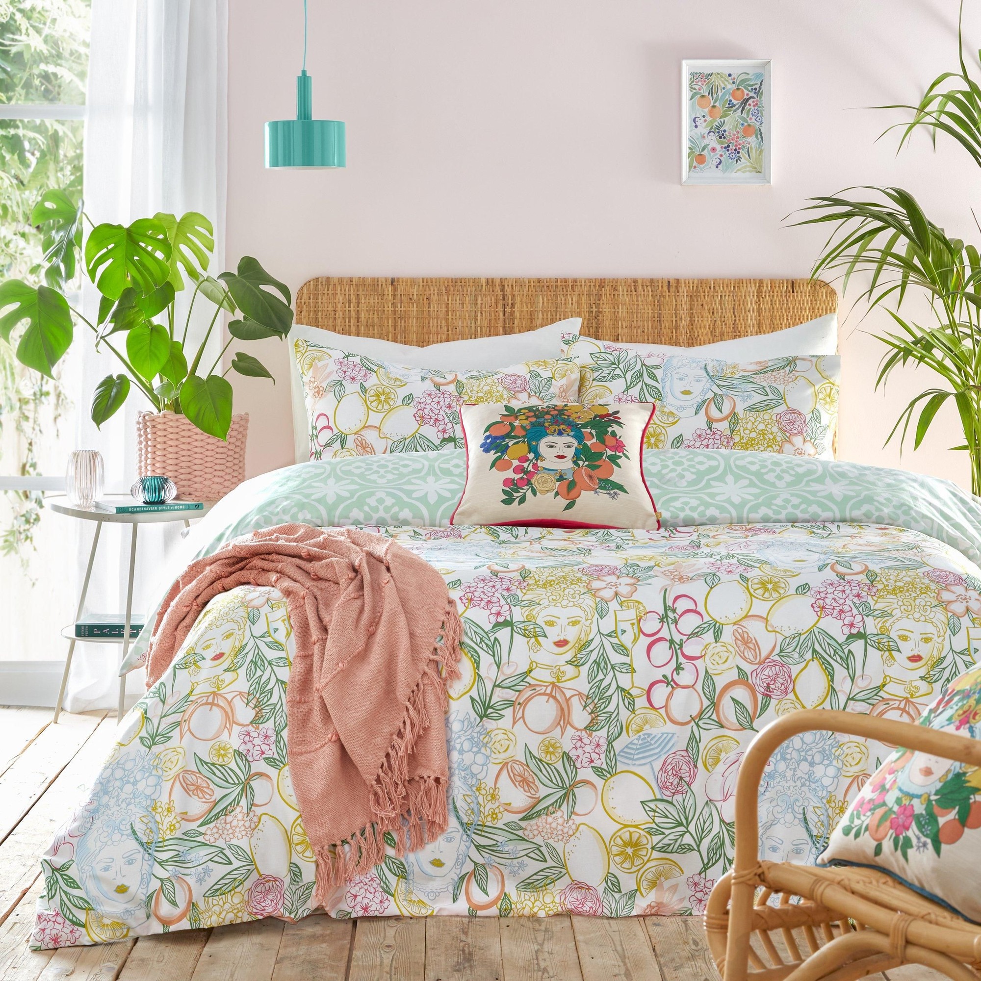Floral duvet cover set featuring vibrant botanical prints in pastel colors, complemented by a pink throw and decorative pillow, set against a light pink wall and natural wood flooring.
