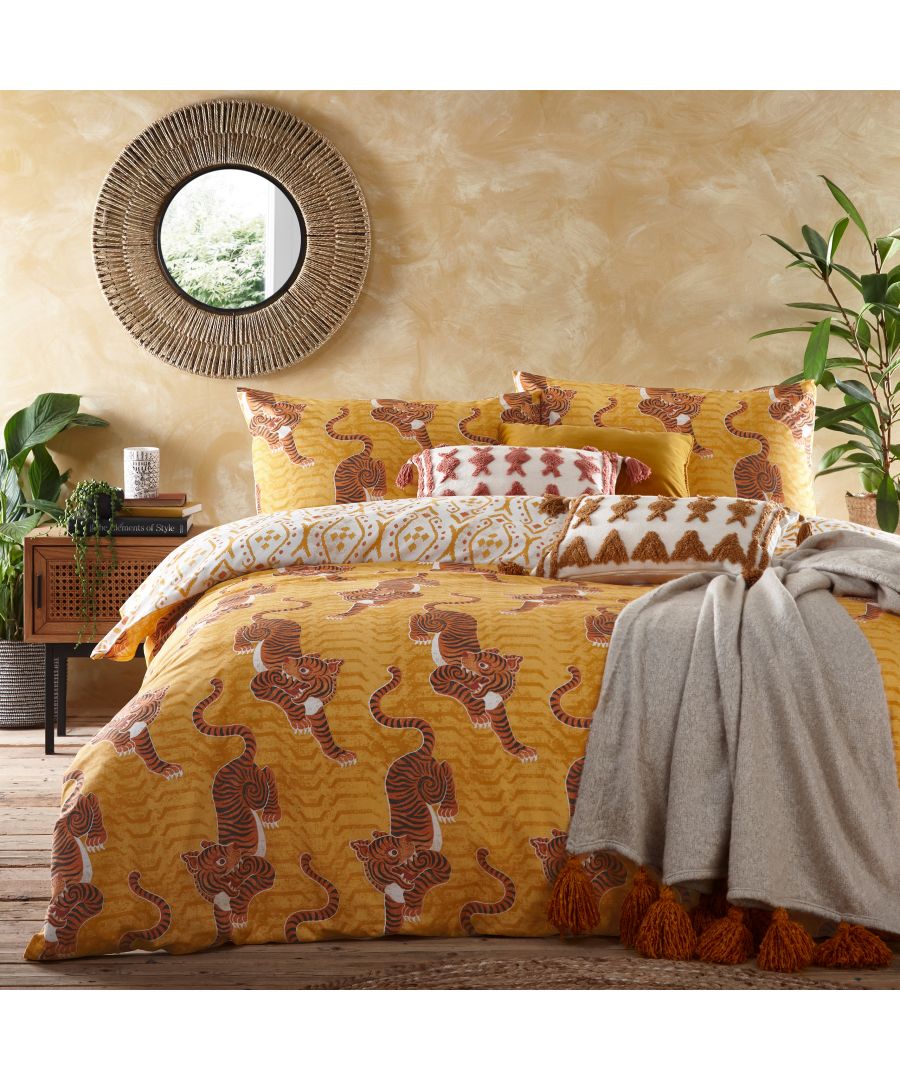 Reversible duvet cover set featuring mustard cotton with tribal Tibetan tiger print, complemented by patterned pillows and a cozy gray throw, set against a warm, textured wall.