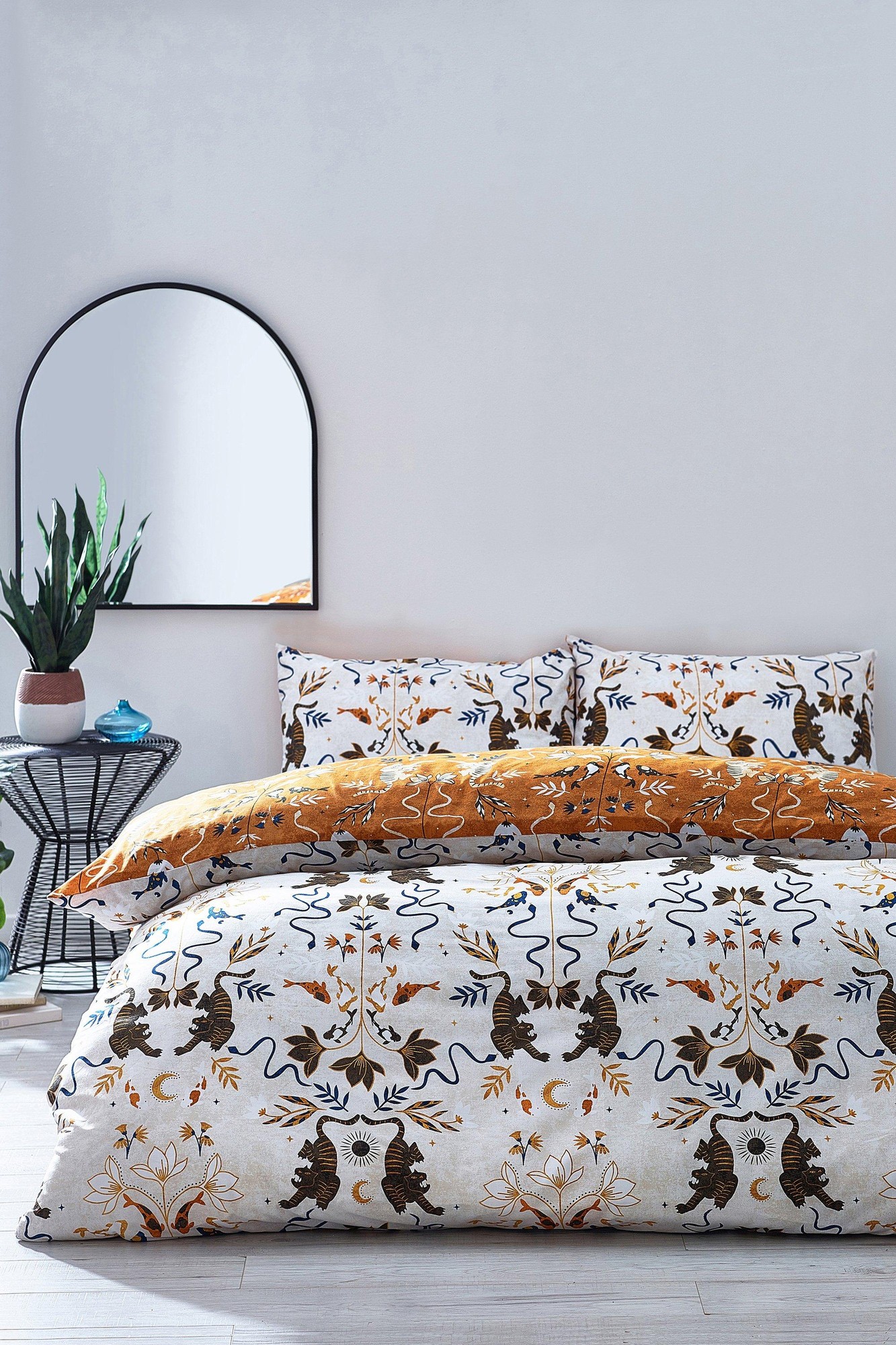 Reversible duvet cover set featuring a botanical tiger fish design in orange and white, complemented by matching pillowcases, with a modern mirror and plant in the background.