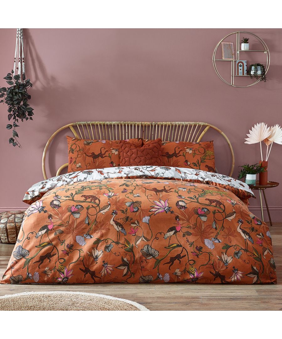Tropical reversible duvet cover set in orange cotton featuring floral patterns, complemented by matching pillowcases, styled on a rattan bed frame against a pink wall.
