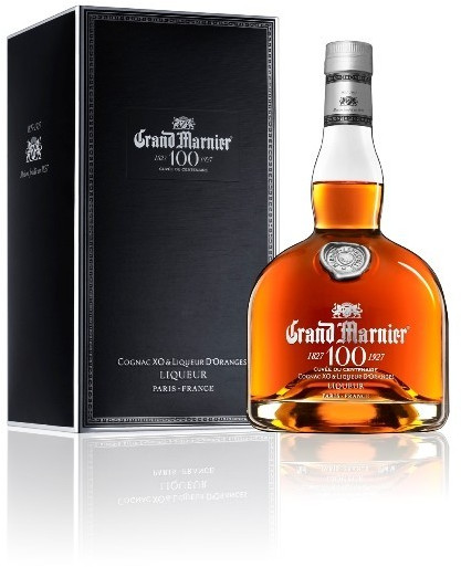 Amber-colored liqueur in an elegant glass bottle with a rounded shape, featuring a silver label and a cork stopper, displayed alongside a sleek black box with silver accents.