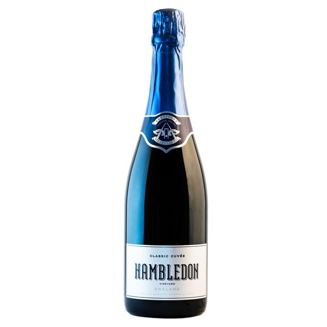 A dark glass bottle of Hambledon Classic Cuvee English Sparkling Wine with a blue foil cap, featuring a white label with elegant black text and a crest logo.